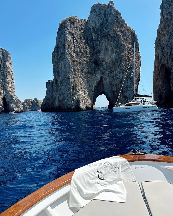 Proa de um barco com uma camiseta branca dobrada, diante dos rochedos Faraglioni em Capri