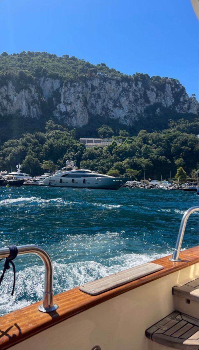 Vista de um barco em movimento passando por um iate ancorado em Capri, com a encosta verde ao fundo