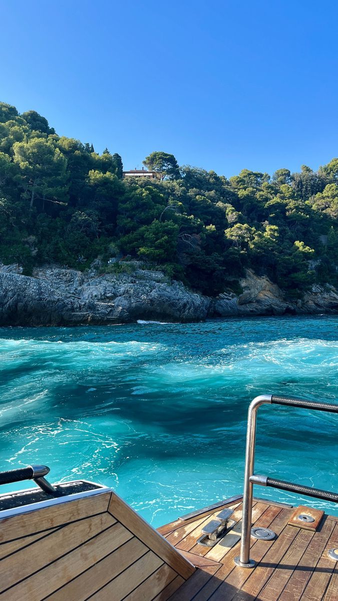 Vista da popa de um barco sobre o mar turquesa, com a costa arborizada ao fundo