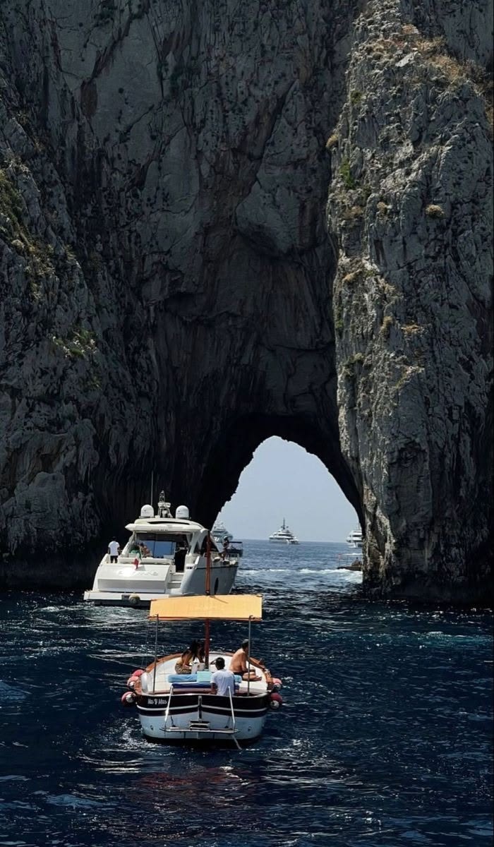 Barcos passando por um grande arco de pedra no mar